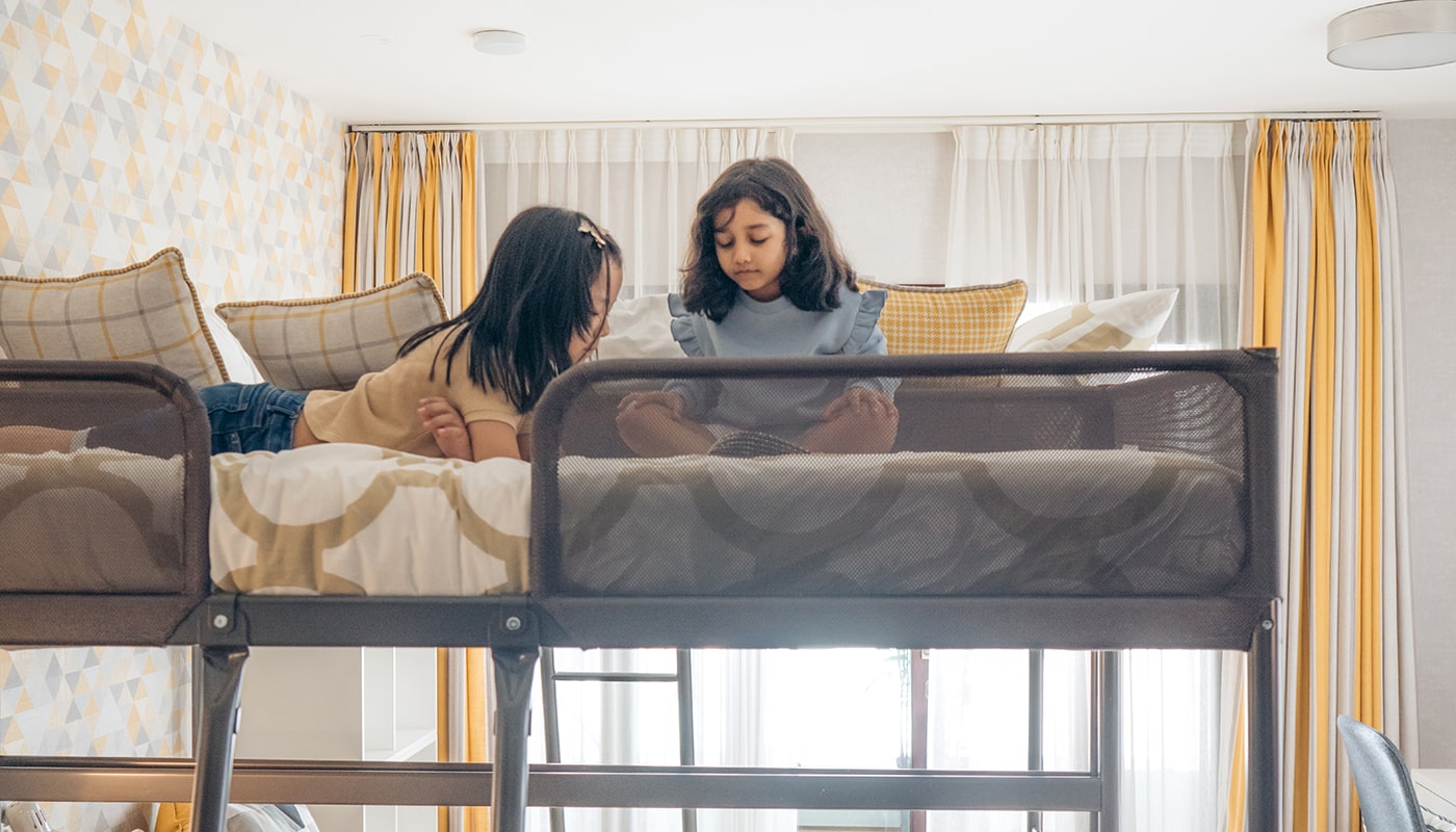 Two young girls reading and bonding on a cozy bunk bed in a sunlit, child-friendly bedroom at Embassy Grove luxury villaments in Bangalore.