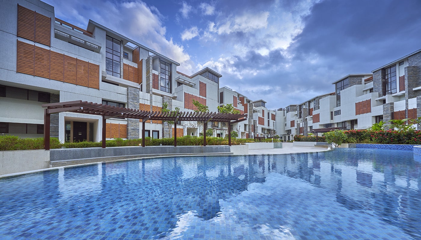 View of Embassy Grove's modern villament residences in Bangalore with expansive central swimming pool, landscaped gardens, and contemporary architecture under a blue sky.