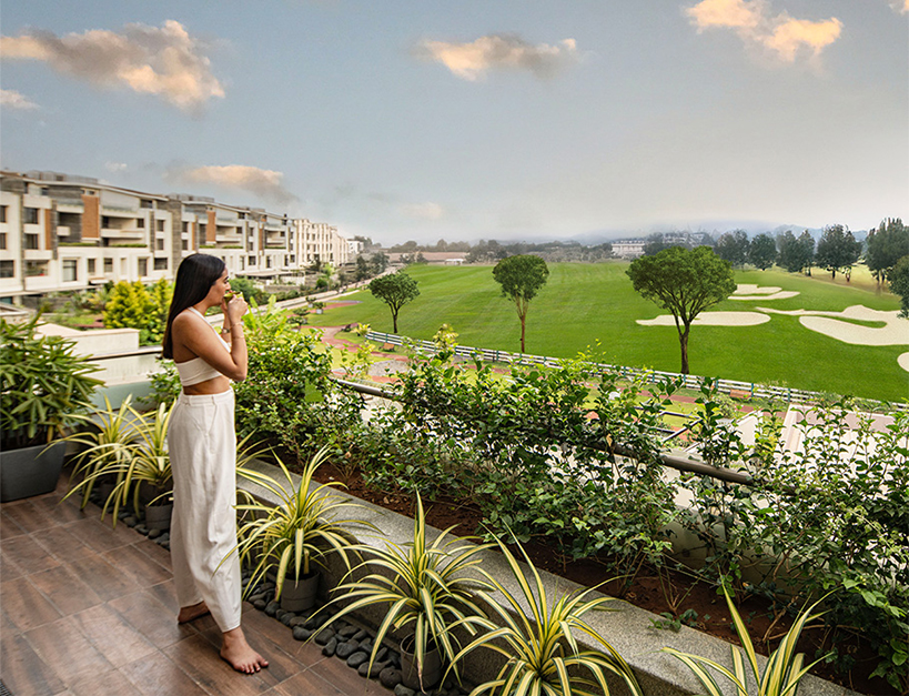 Woman enjoying a serene morning view of the world-class golf course from the balcony of a luxury Embassy Grove villament in Bangalore.