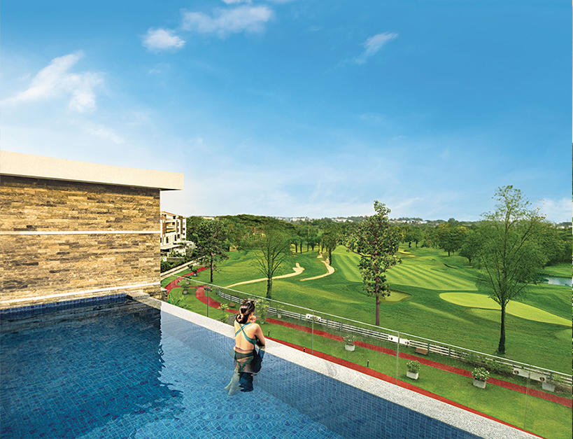 Woman relaxing in a private rooftop pool at Embassy Grove, overlooking a stunning green golf course under a clear blue sky in Bangalore